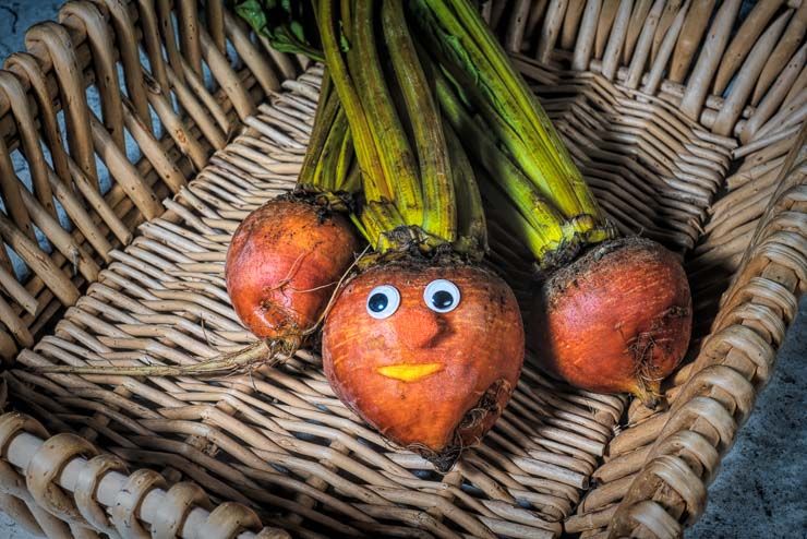 three golden beets (root vegetables) arranged in a basket. the center beet has a pair of googly eyes with a smiling mouth cut into the beet.