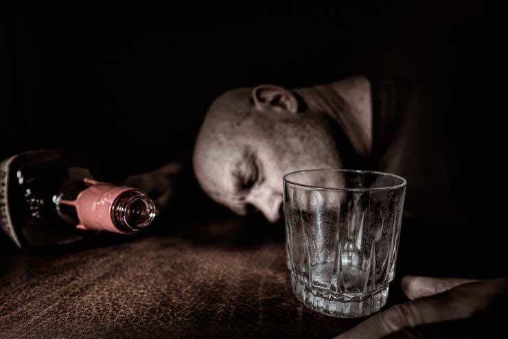 man passed out on floor with empty glass and empty whisky bottle