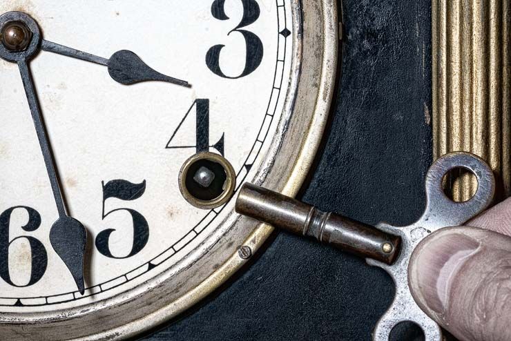 closeup of an antique mantle clock face. a key is held near the keyhole on the clock face to set the time